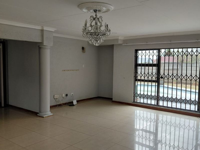 Spacious living area featuring large format floor tiles, a decorative ceiling rose with a crystal chandelier, and direct access to the pool area.