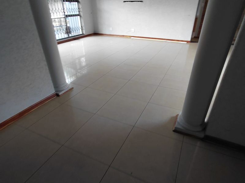 Spacious, empty living area featuring large porcelain floor tiles, decorative columns, and a central chandelier, offering a blank canvas for interior design.
