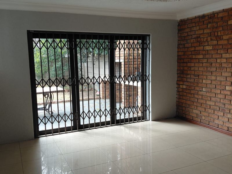 Spacious living area featuring an exposed brick wall, tiled flooring, ornate ceiling detailing, and a sliding door with security gate leading to the patio.
