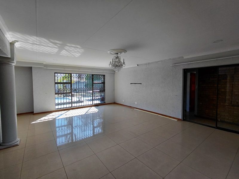 Spacious, empty living area featuring large porcelain floor tiles, a decorative chandelier, and a security gate leading to the outdoor pool area.