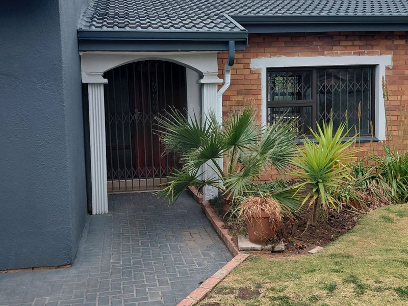 Front entrance of a brick house featuring a paved walkway, security gate, and decorative columns under a tiled roof.