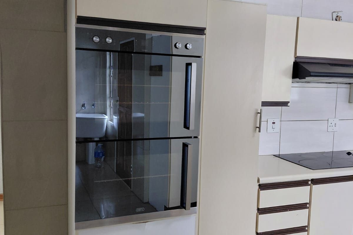A functional kitchen featuring built-in double oven, electric hob, extractor fan, and tiled finishes with ample cabinetry for storage.