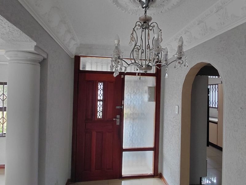 Welcoming entrance hall featuring tiled flooring, an ornate ceiling rose with chandelier, decorative cornicing, and a classic timber front door with glass sidelight.
