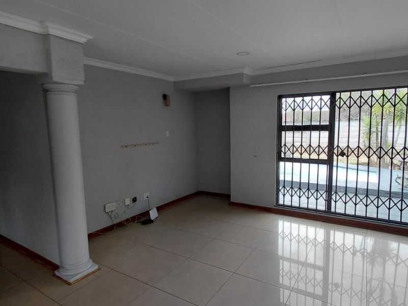 Spacious living area featuring large porcelain floor tiles, a decorative column, and a sliding glass door with security gate leading to the pool area.