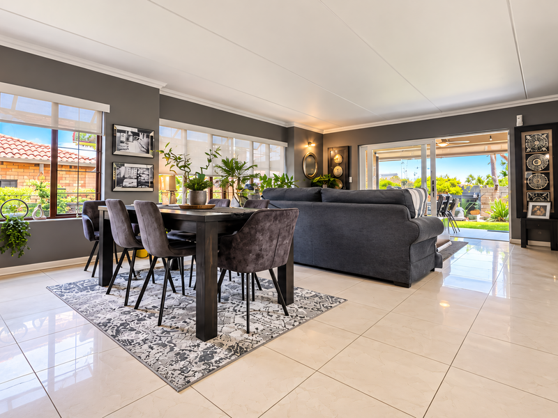 Spacious open-plan living and dining area featuring polished tiled floors, large windows, and seamless access to the outdoor patio through sliding glass doors.
