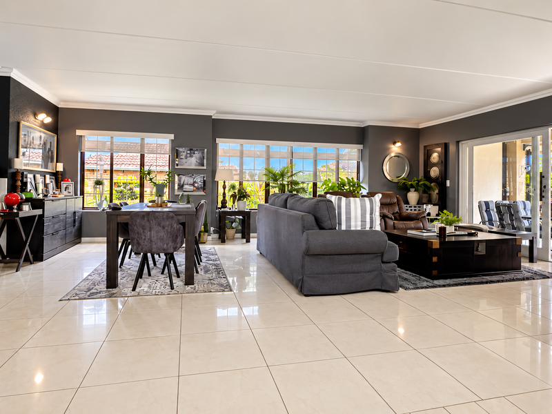 Spacious open-plan living and dining area featuring polished tile flooring, modern dark accent walls, and large sliding glass doors leading to an outdoor patio.