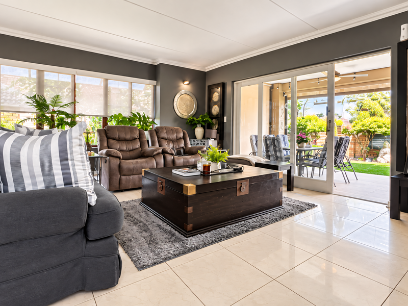 Spacious living room featuring large format floor tiles, modern grey wall finishes, and seamless access to an outdoor patio through sliding glass doors.