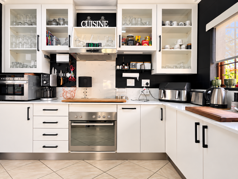 Modern kitchen featuring white cabinetry, stone countertops, marble-look splashback, built-in oven, and extractor fan, complemented by contrasting black wall tiles.
