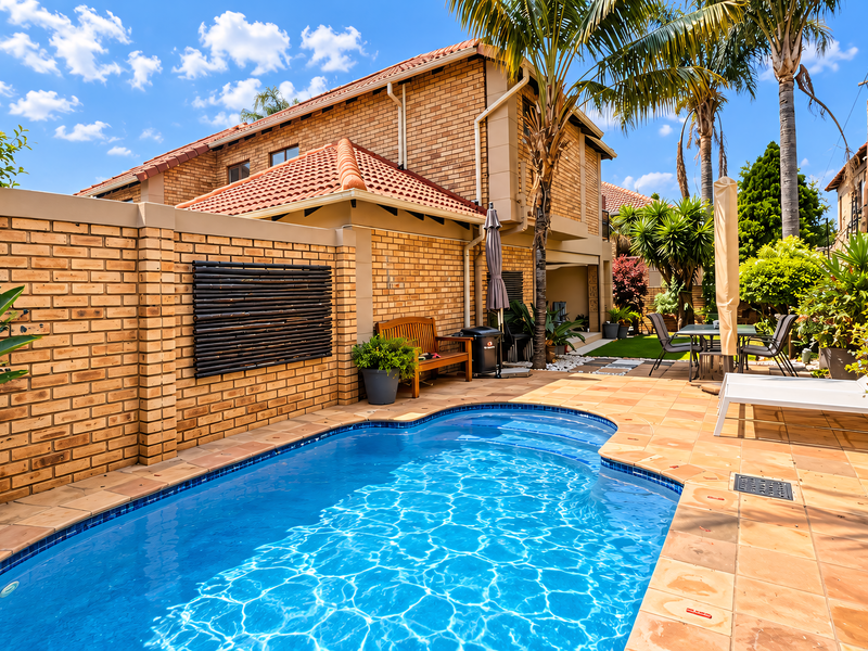A well-maintained outdoor pool area featuring a private swimming pool, paved patio space, and brick boundary walls within a townhouse setting.