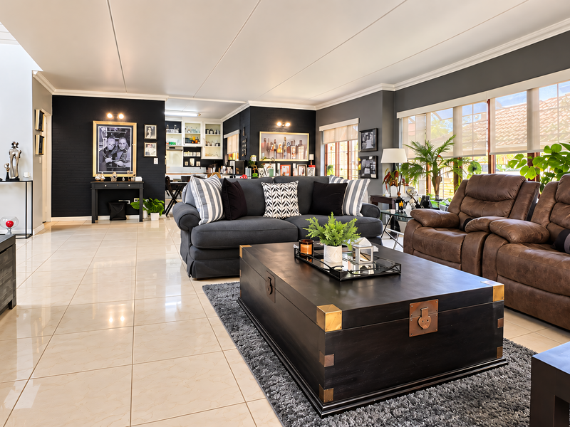 Spacious open-plan living area featuring polished tiled flooring, neutral walls with a dark accent wall, and abundant natural light through large windows.