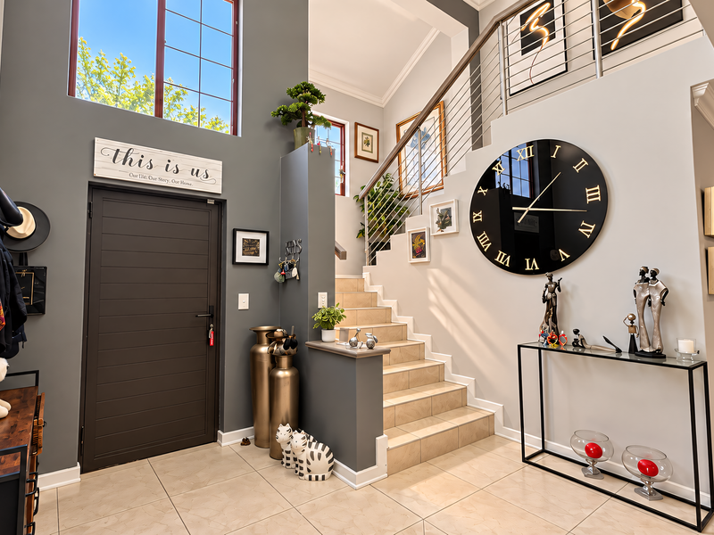 Spacious double-volume entrance hall featuring tiled flooring, a modern staircase with stainless steel balustrades, and a large feature window.