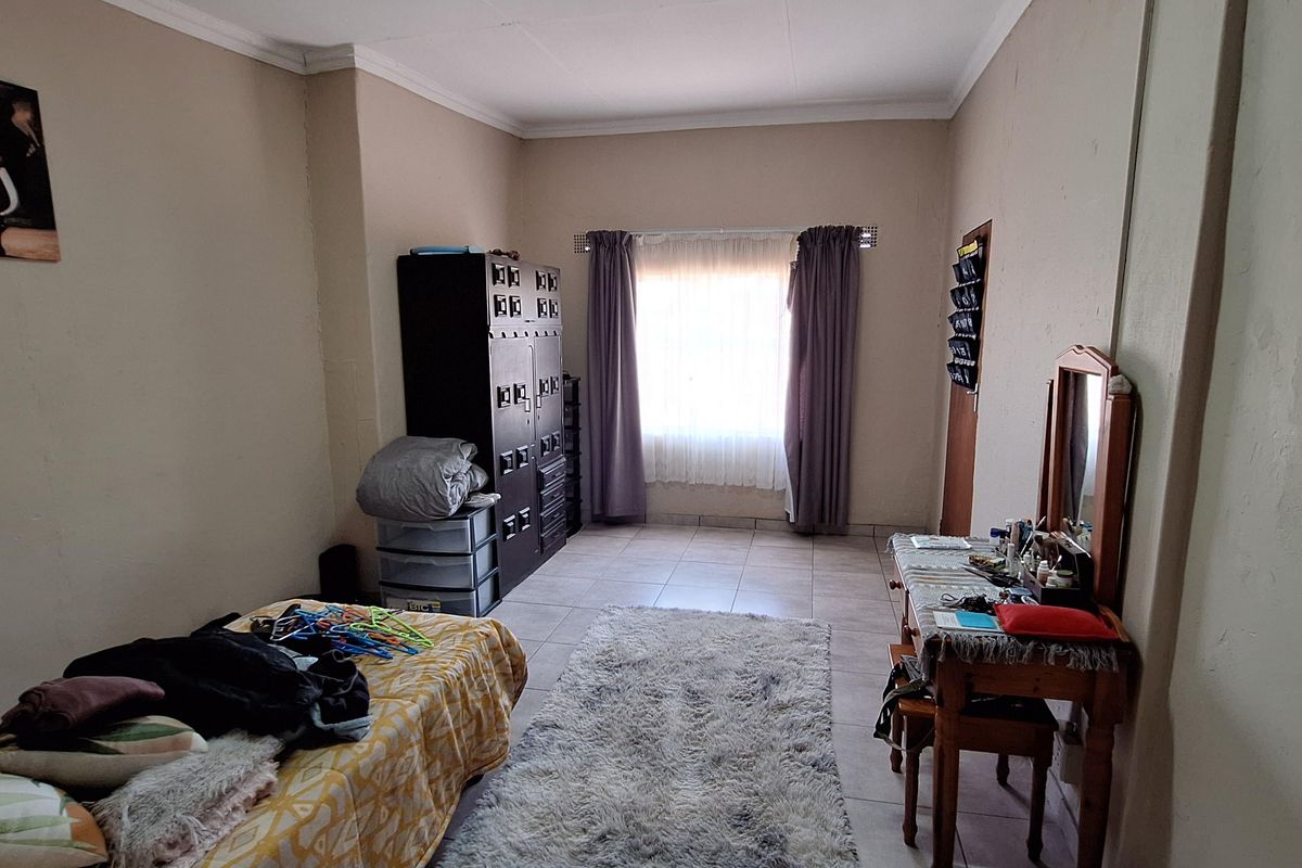 A functional bedroom featuring tiled flooring, neutral wall tones, and a window with curtains, providing a simple and practical living space.