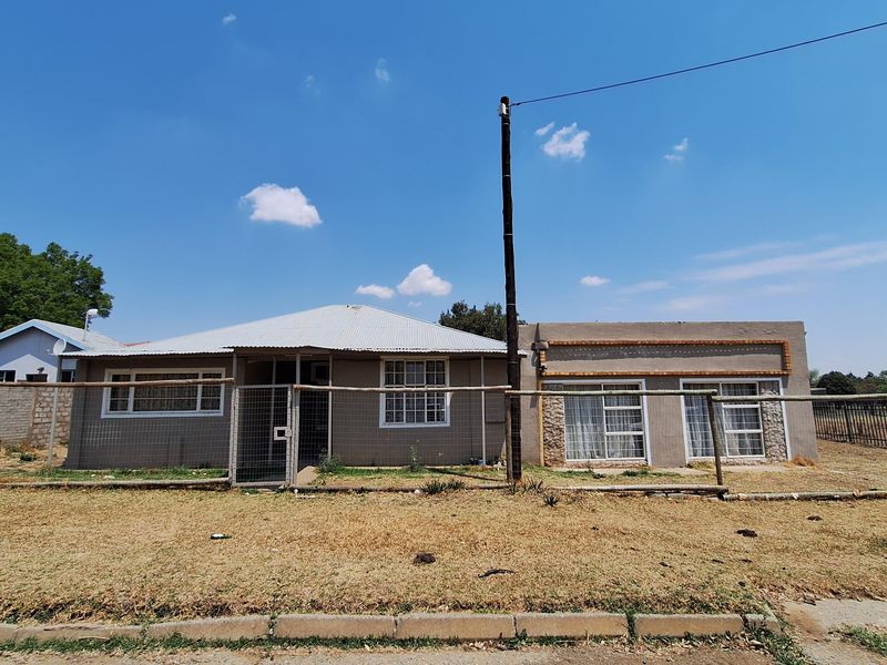 Front elevation of a single-story house featuring a corrugated metal roof, plaster finish, and a fenced yard area.