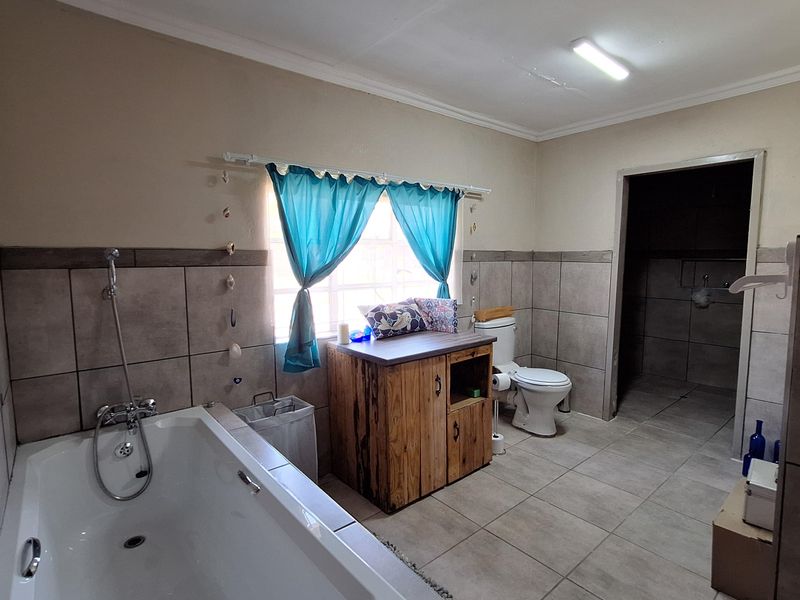 A functional bathroom featuring a built-in bathtub, tiled walls, and a vanity unit, with an adjacent utility area visible through the doorway.
