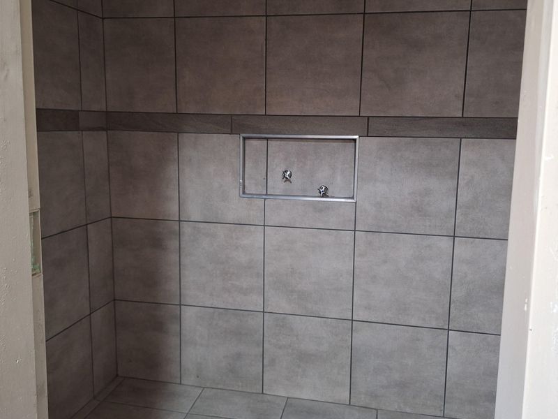 A modern walk-in shower enclosure featuring large-format grey wall and floor tiles, a built-in wall niche, and a fixed overhead shower head.
