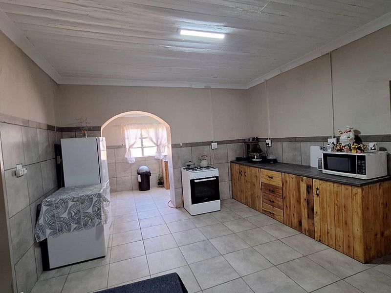 Functional kitchen featuring tiled flooring, wooden cabinetry, a freestanding stove, and an arched doorway leading to an adjacent utility area.