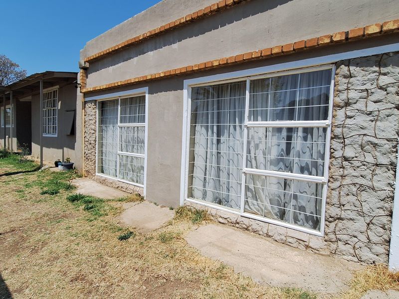 Exterior view of the house featuring stone cladding accents, large windows with security bars, and a concrete pathway leading along the building.
