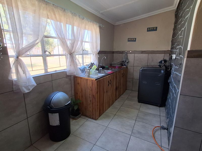 A functional laundry area featuring tiled flooring, wall tiling, a built-in wooden sink cabinet, and a window providing natural light.