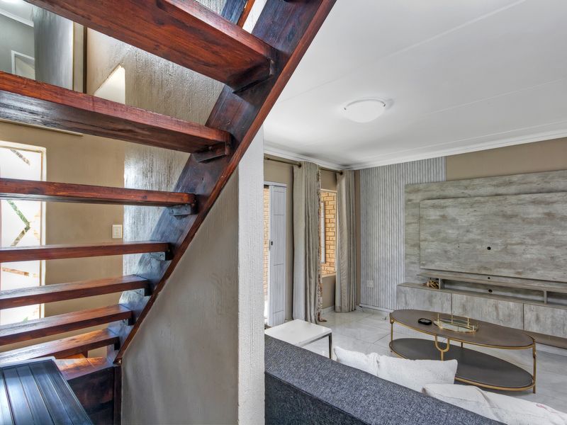 A well-lit living room featuring a prominent wooden staircase, tiled flooring, and a custom built-in media unit with a modern aesthetic.