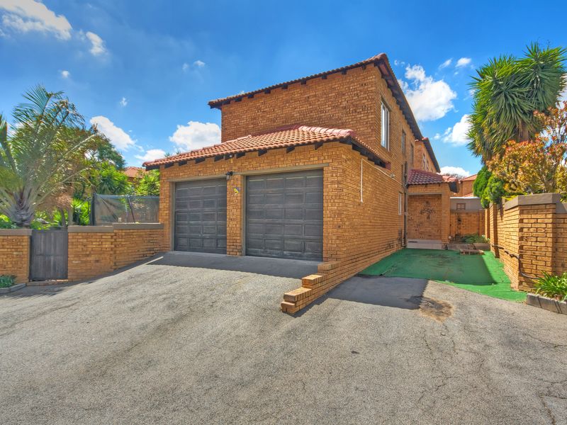 Front exterior view of a double-story townhouse featuring a double garage, brick facade, tiled roof, and an asphalt driveway.