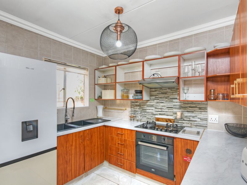 A well-maintained kitchen featuring wood-finish cabinetry, stone-look countertops, a gas hob, built-in oven, and a modern tiled backsplash.