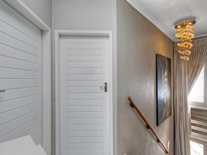 A well-lit hallway featuring textured walls, a wooden handrail, and multiple internal doors, leading towards a staircase area.