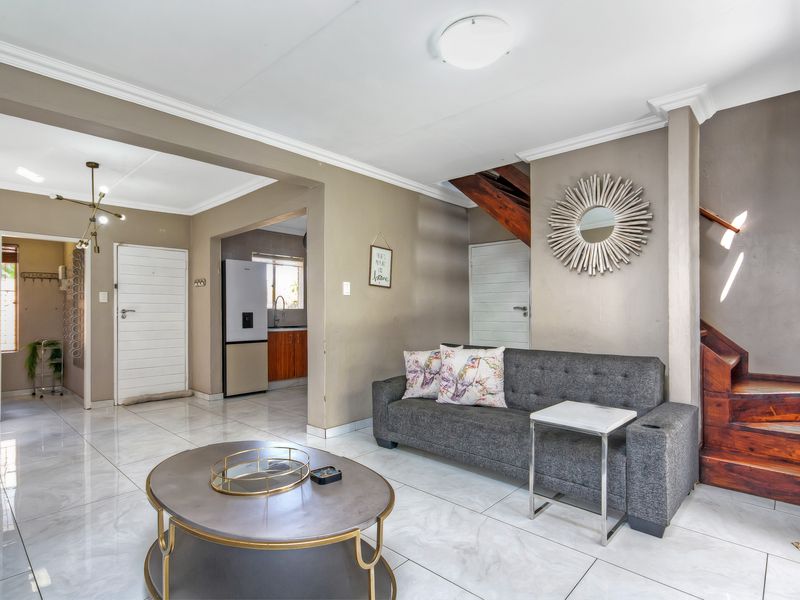 Open plan living area featuring tiled flooring, a wooden staircase, and neutral wall tones, providing a functional and connected layout.