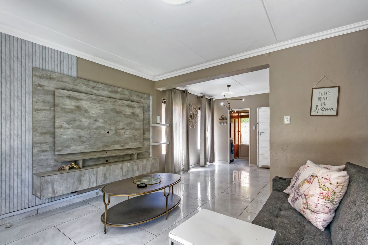 A well-maintained living room featuring a modern built-in media unit, polished tiled flooring, and crown molding, leading into an adjacent hallway area.