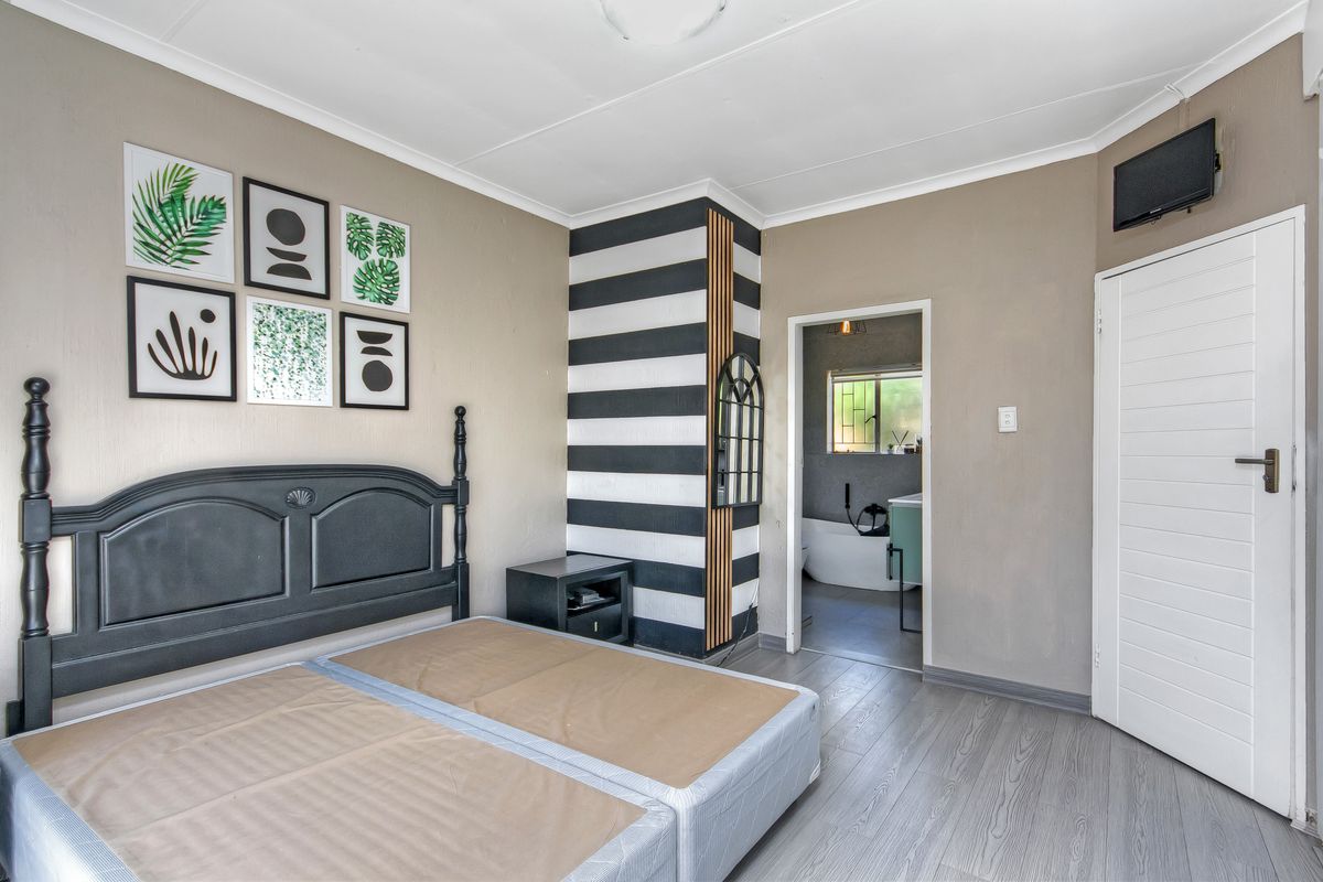 A bedroom featuring laminate flooring and an en-suite bathroom access point, with neutral wall tones and a decorative feature column.