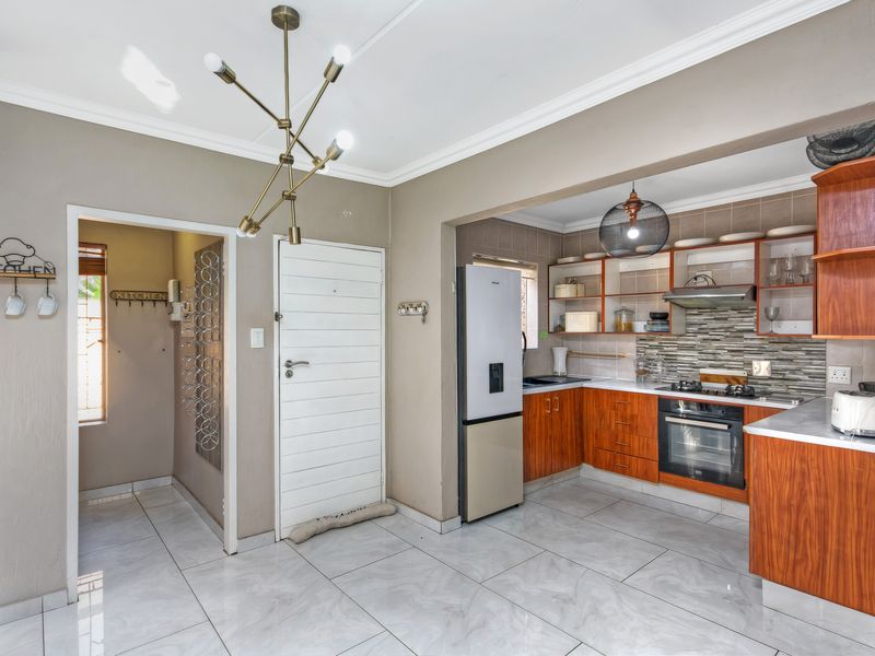 A functional kitchen featuring wood-finish cabinetry, a gas hob with extractor, tiled flooring, and an adjacent utility area with direct access.