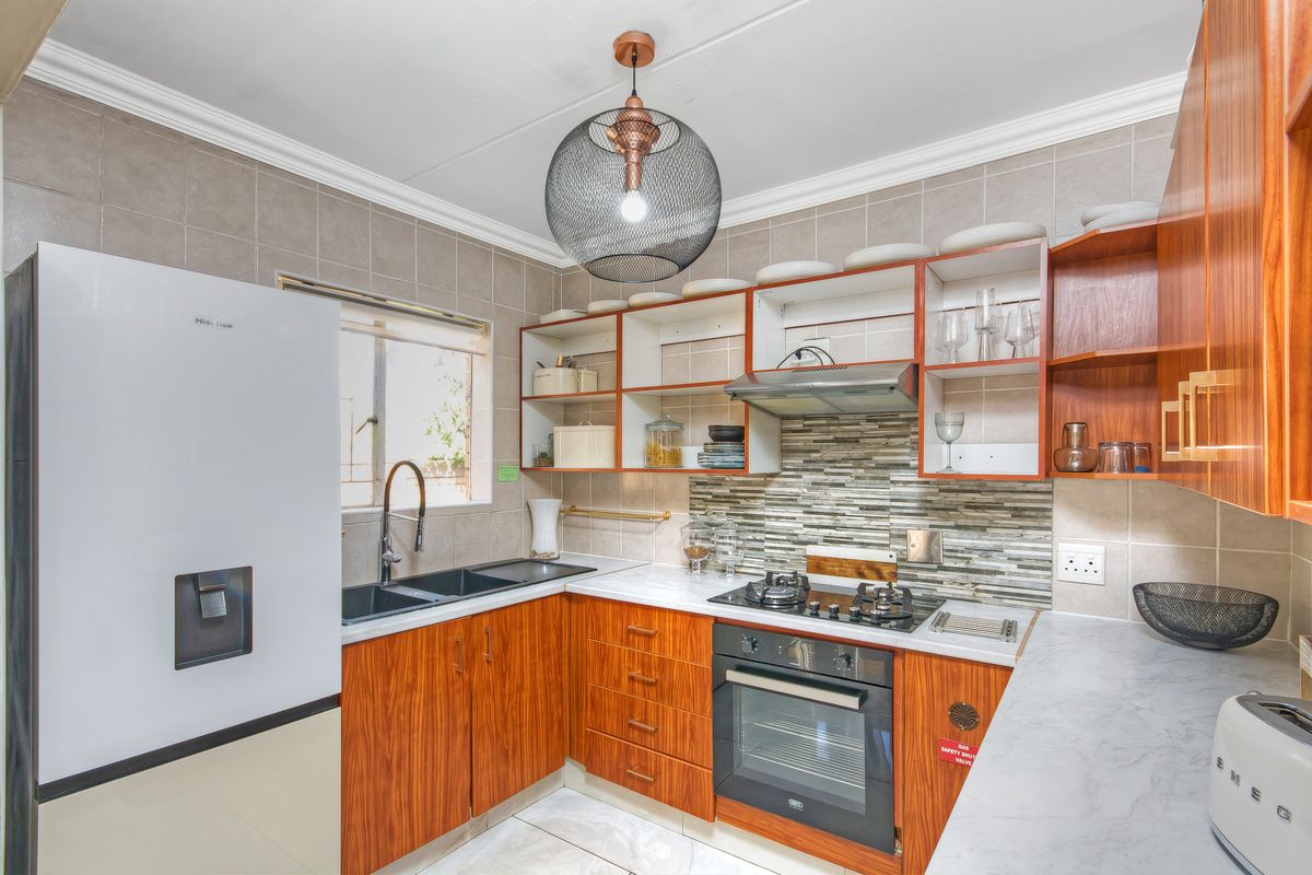 A well-maintained kitchen featuring wood-finish cabinetry, stone-look countertops, a gas hob, built-in oven, and a modern tiled backsplash.
