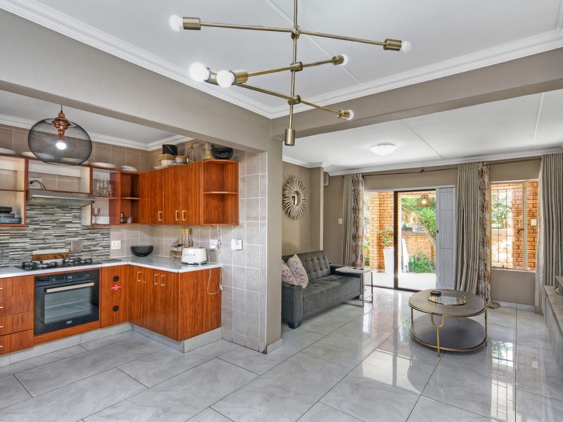 Open-plan living area featuring a modern kitchen with wooden cabinetry, gas hob, and tiled flooring, seamlessly flowing into a bright lounge with patio access.