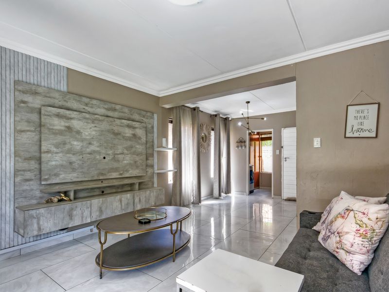 A well-maintained living room featuring a modern built-in media unit, polished tiled flooring, and crown molding, leading into an adjacent hallway area.