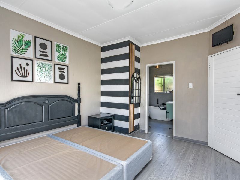 A bedroom featuring laminate flooring and an en-suite bathroom access point, with neutral wall tones and a decorative feature column.