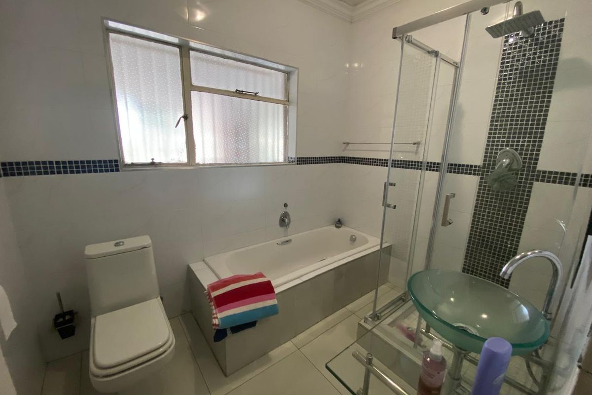 A functional bathroom featuring a built-in bathtub, separate glass shower enclosure, and a modern glass basin with tiled finishes throughout.