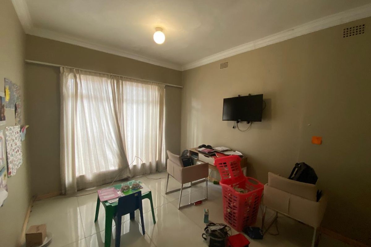 A living room featuring tiled flooring, ceiling cornices, and wall-mounted television infrastructure, currently requiring cosmetic updates and wall repairs.