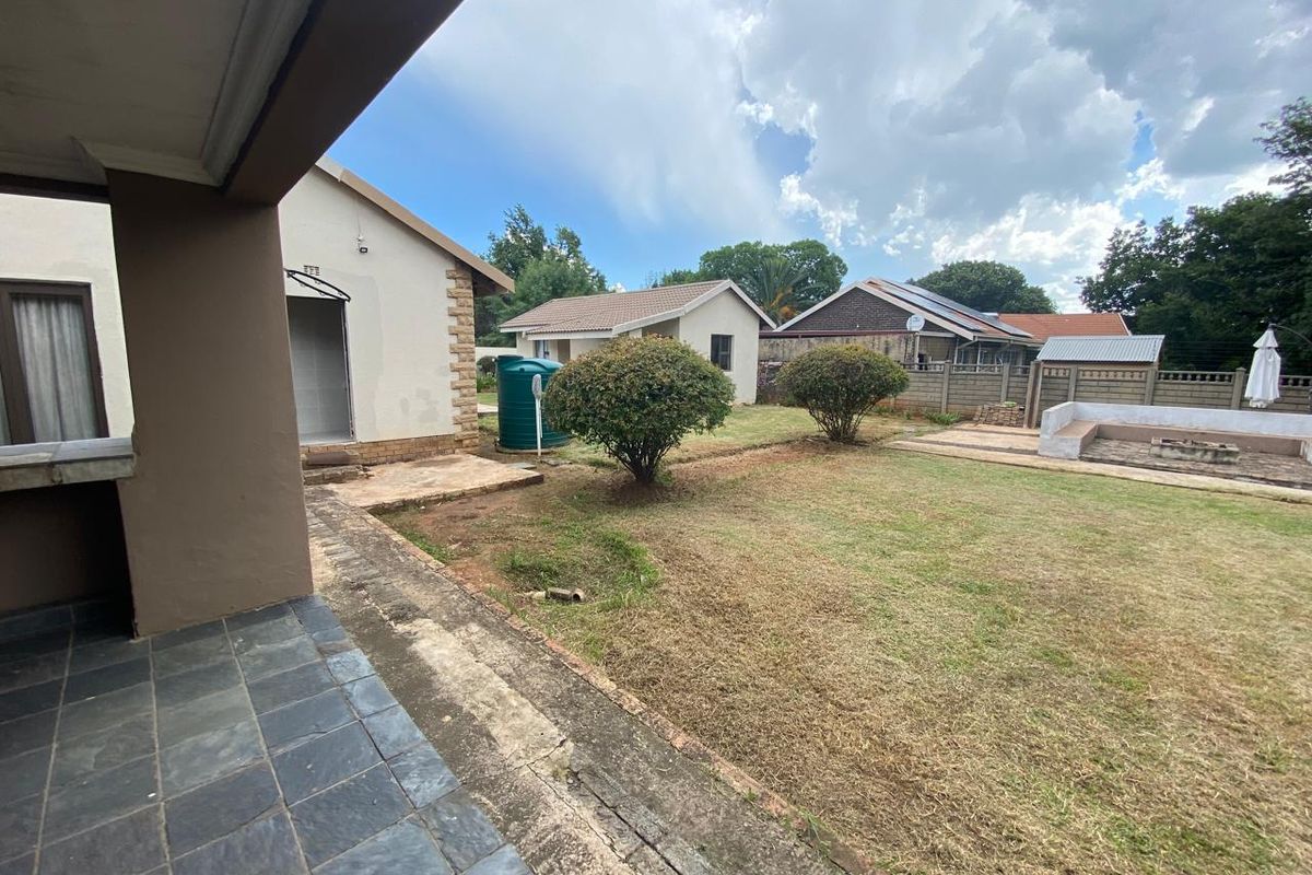 Spacious rear garden featuring a tiled patio, built-in braai area, and a water tank, offering potential for outdoor landscaping and entertainment.