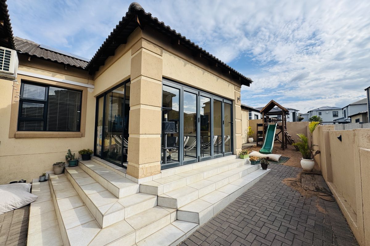 Rear exterior view featuring a tiled patio with aluminium stacker doors, paved flooring, and a surrounding boundary wall.