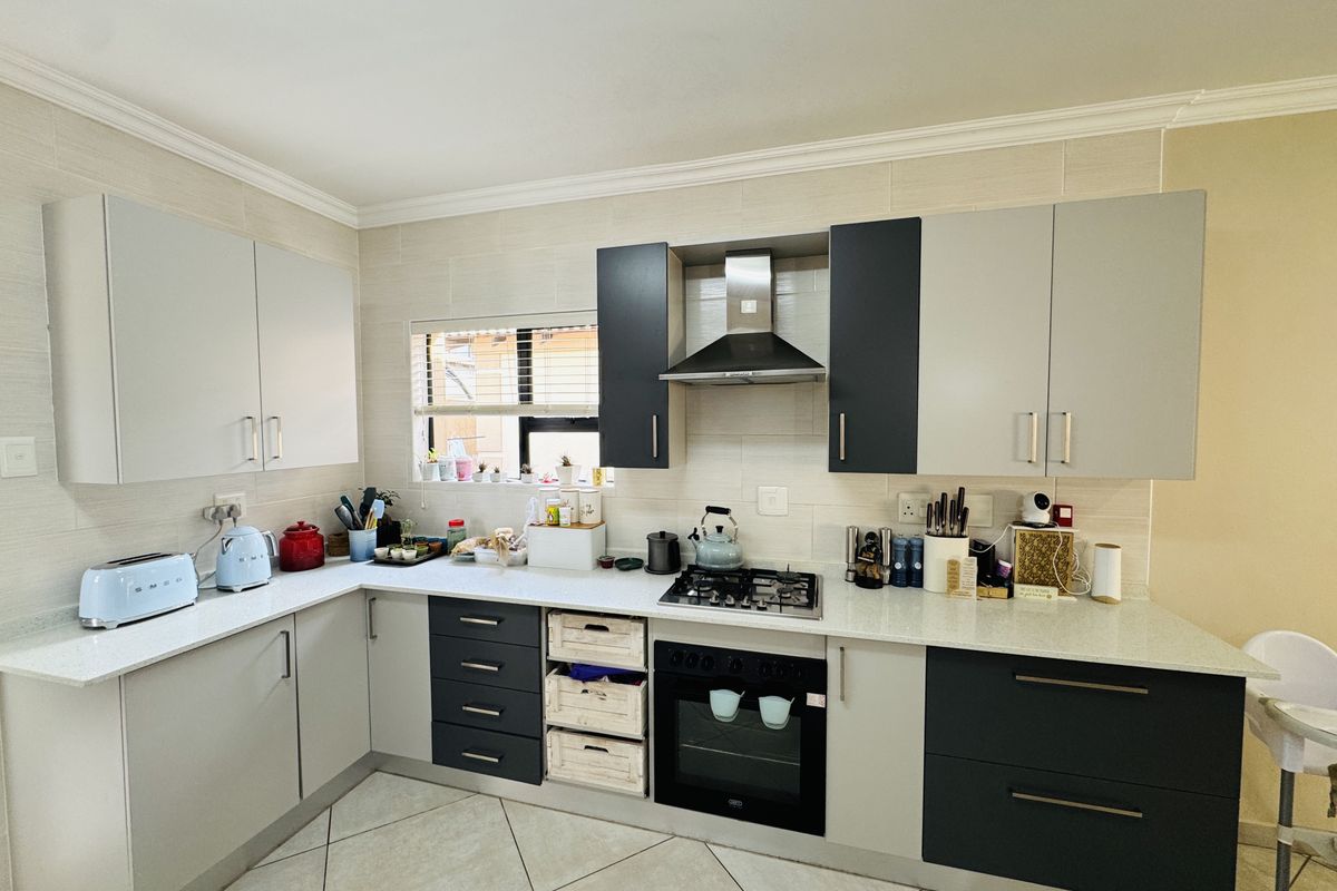 Modern kitchen featuring two-tone cabinetry, stone countertops, built-in gas hob, oven, and extractor fan with a tiled backsplash and floor.