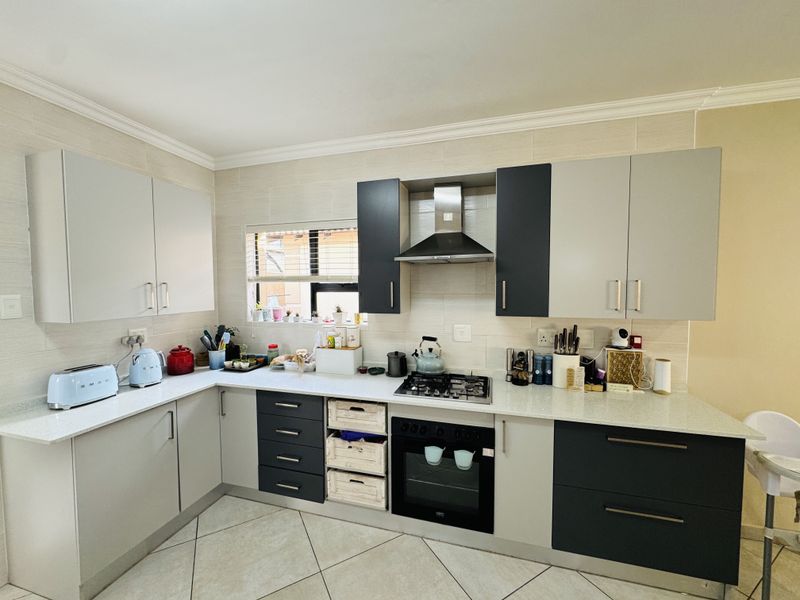 Modern kitchen featuring two-tone cabinetry, stone countertops, built-in gas hob, oven, and extractor fan with a tiled backsplash and floor.