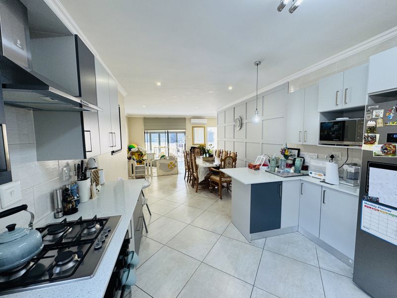 Spacious open-plan kitchen and dining area featuring modern cabinetry, stone countertops, integrated appliances, and elegant wall paneling with tiled flooring throughout.