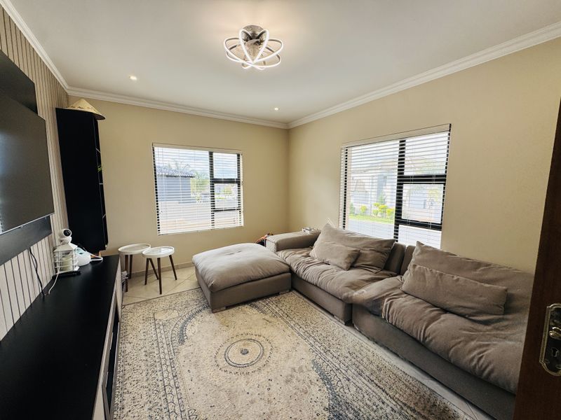 A well-maintained living room featuring tiled flooring, modern ceiling lighting, and large windows with venetian blinds, offering a bright and comfortable living space.