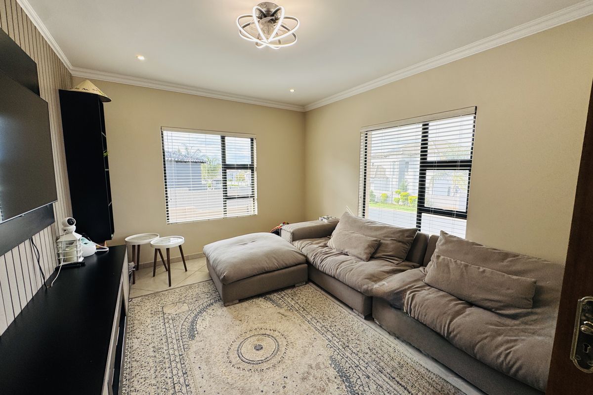 A well-maintained living room featuring tiled flooring, modern ceiling lighting, and large windows with venetian blinds, offering a bright and comfortable living space.