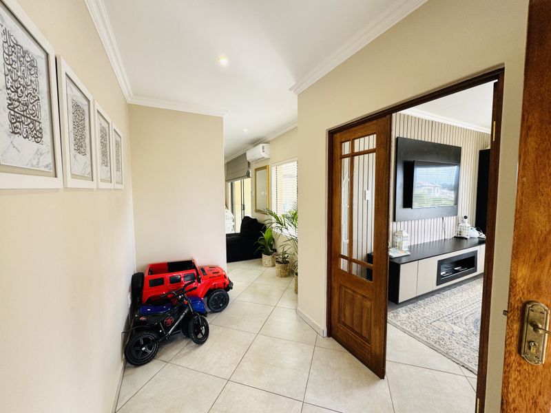 A bright, tiled hallway featuring coved cornicing and a timber-framed glass door leading into an adjacent living space.