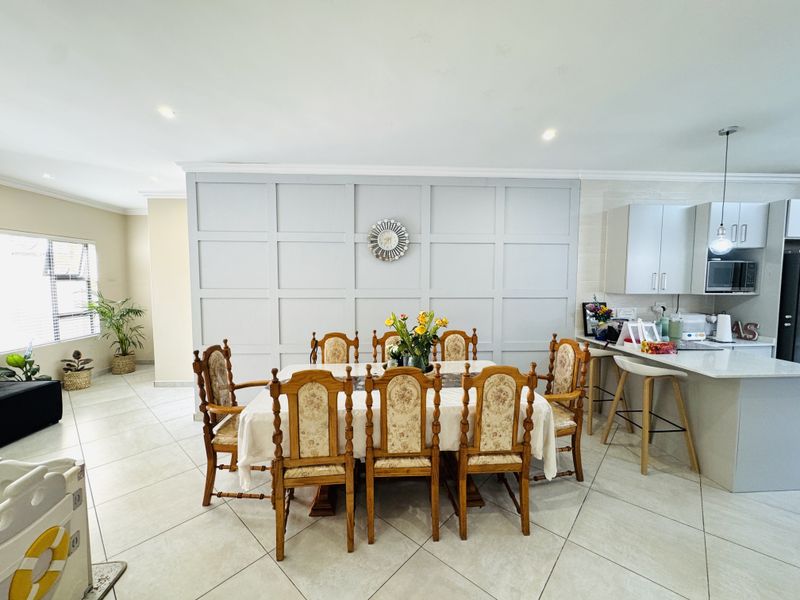 Spacious open-plan dining and kitchen area featuring a decorative wainscoting feature wall, modern cabinetry, and large format floor tiles.