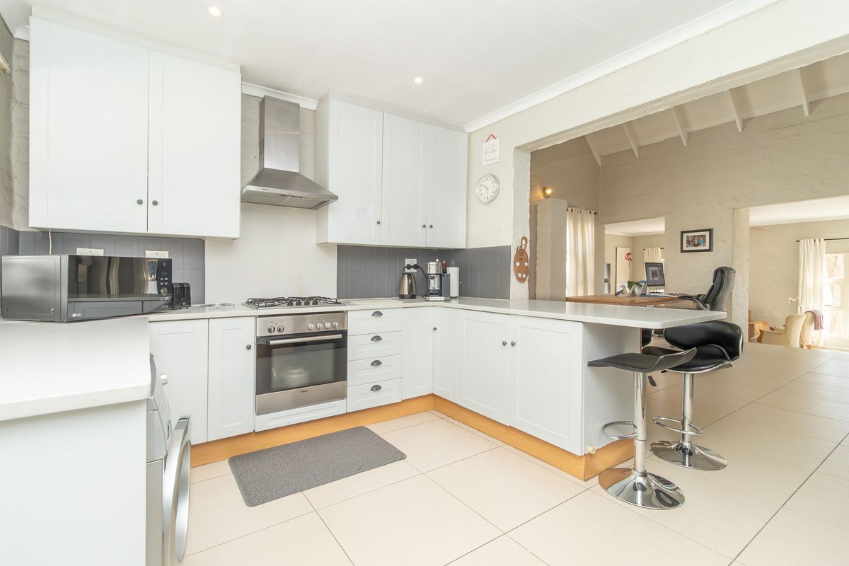 A bright, functional kitchen featuring white cabinetry, a gas hob, stainless steel extractor, and a breakfast bar, seamlessly flowing into the adjacent living area.