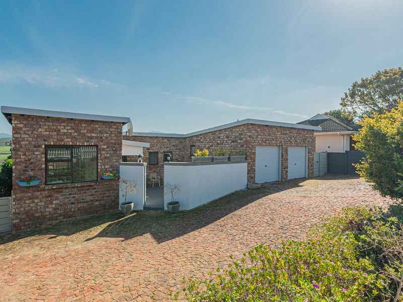 Front exterior view of a brick-faced house featuring a paved driveway, double garage with roller doors, and a low boundary wall.