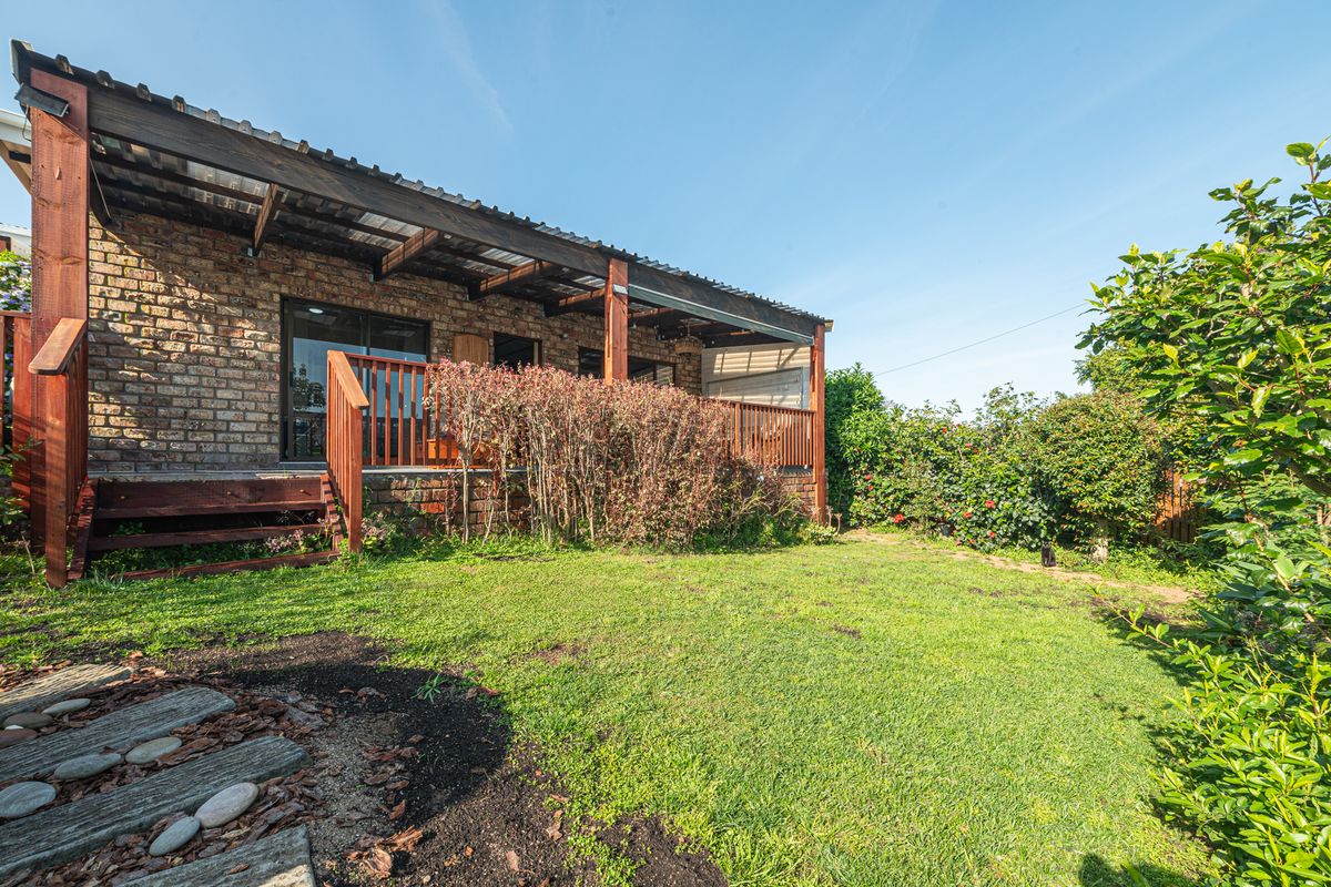 Rear view of the property featuring a brick facade, a raised timber deck with a pergola, and a private garden area.