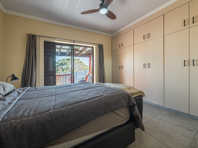 A bedroom featuring built-in cupboards, tiled flooring, a ceiling fan, and a sliding glass door providing access to an outdoor patio area.