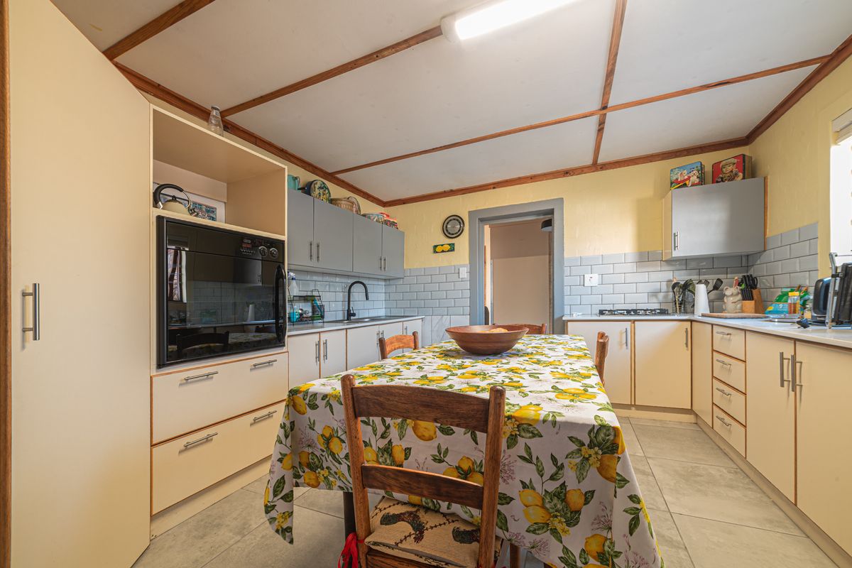 A functional kitchen featuring built-in cabinetry, subway tile backsplash, integrated oven, gas hob, and tiled flooring with exposed timber ceiling beams.